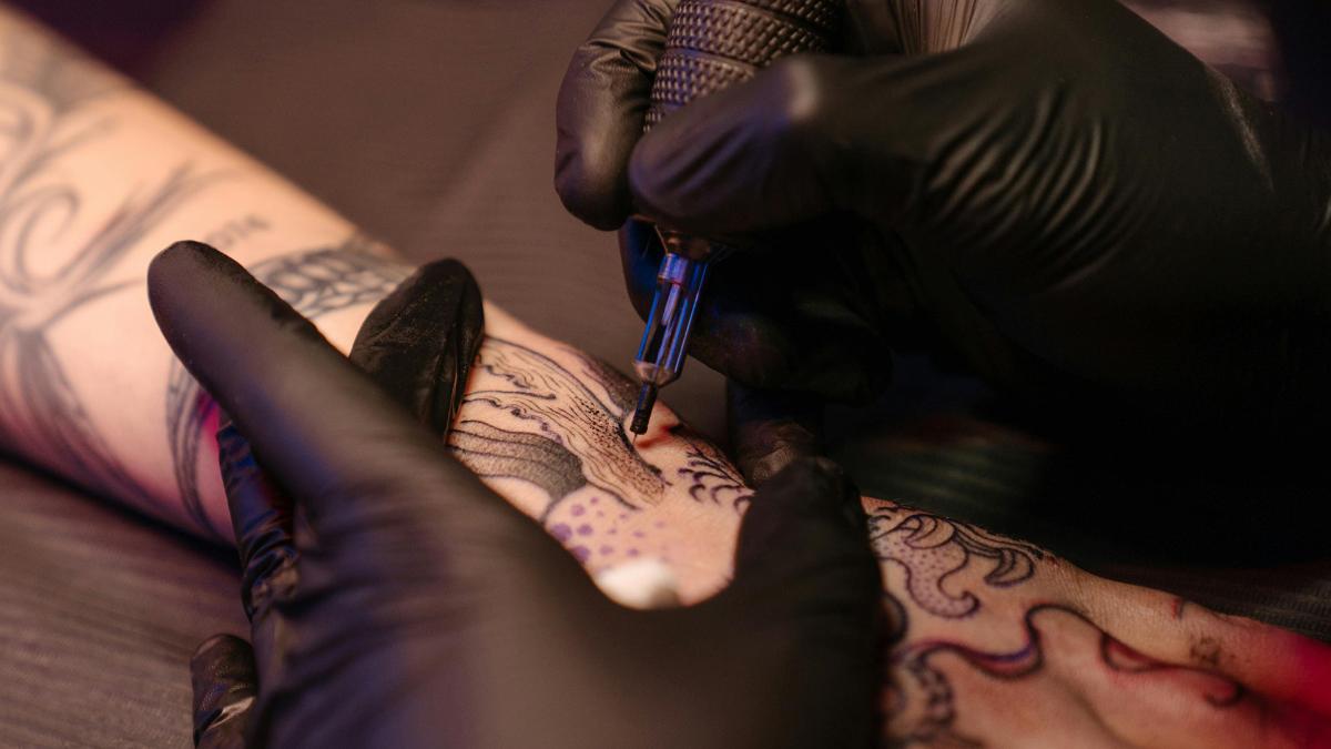 Tatuointineula ihmisen iholla. Tatuoijalla kädessään suojakäsineet.