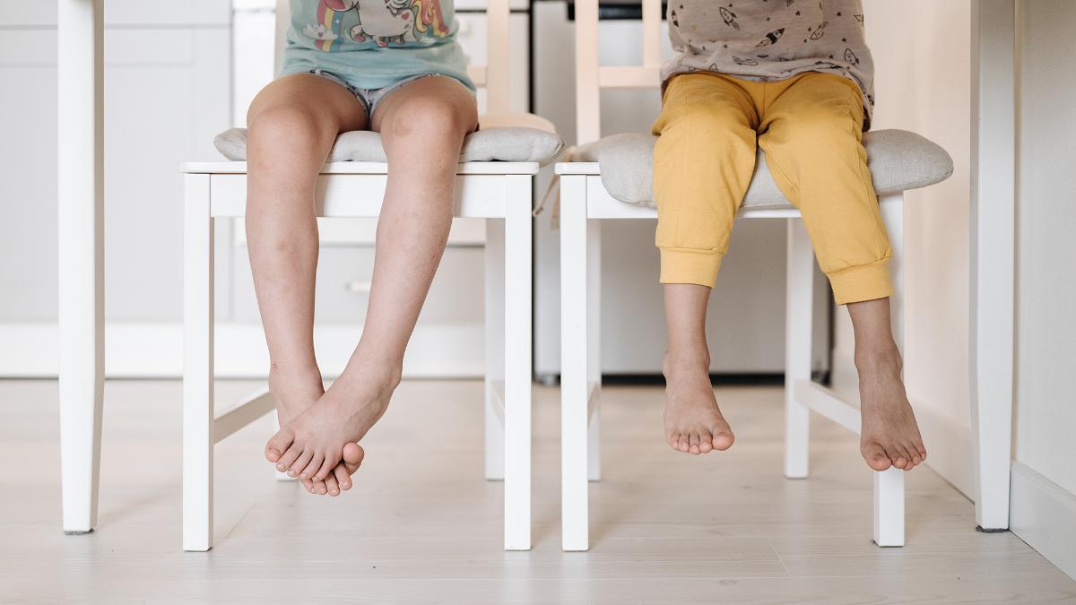 Two children are sitting on chairs, only their feet are visible at the picture.