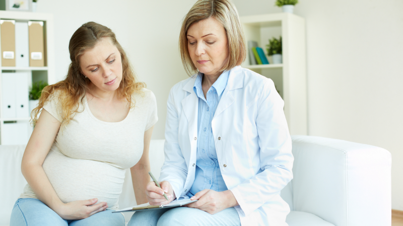 En gravid kvinna och en vårdare samtalar.