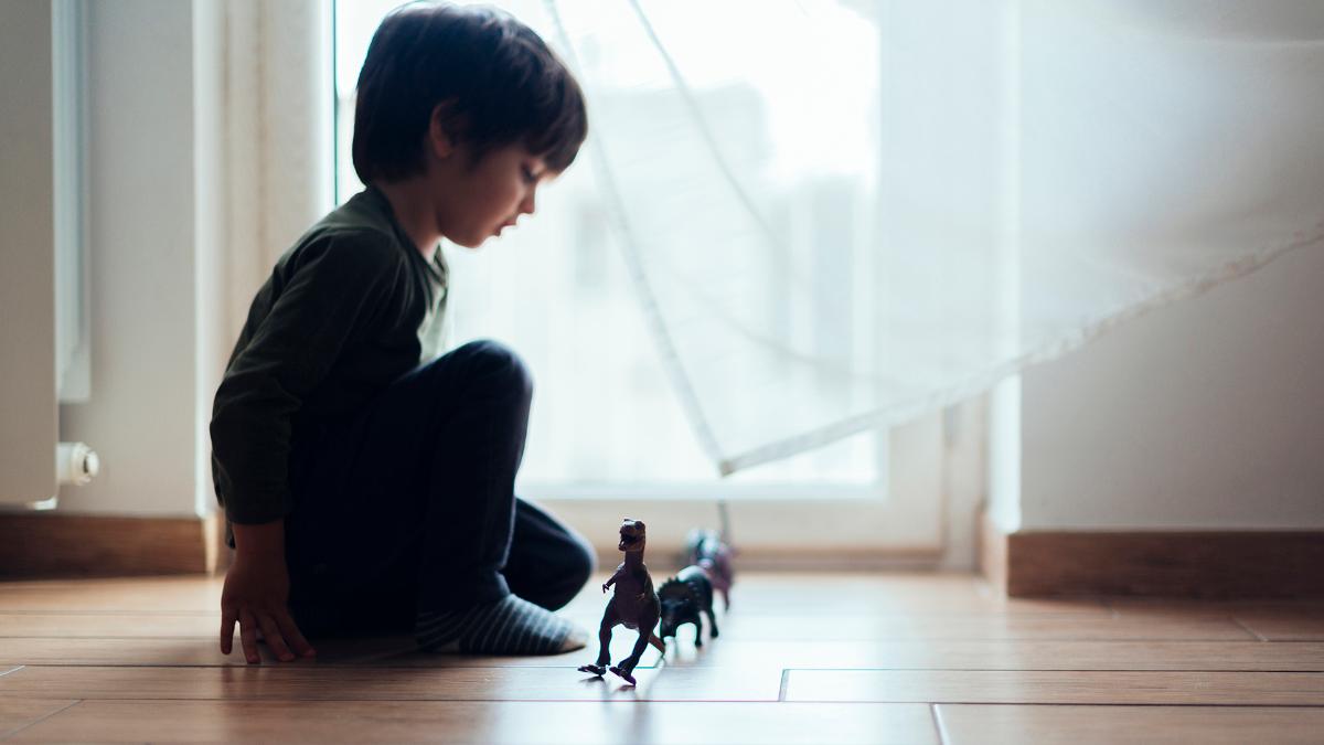 A child and dinosaur toys on the floor.